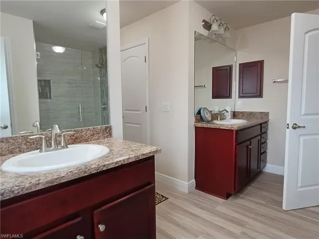 Full bathroom featuring a shower stall, two vanities, and light wood-style flooring