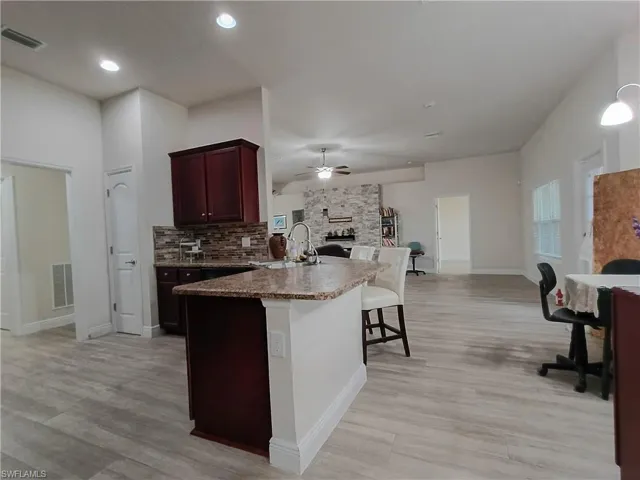 Kitchen featuring a peninsula, a stone fireplace, a kitchen breakfast bar, light wood-style flooring, and recessed lighting