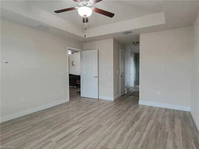Unfurnished bedroom featuring a tray ceiling, a ceiling fan, and light wood finished floors