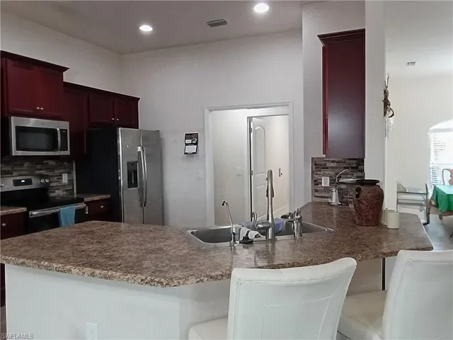 Kitchen featuring appliances with stainless steel finishes, a peninsula, a kitchen breakfast bar, dark brown cabinets, and tasteful backsplash
