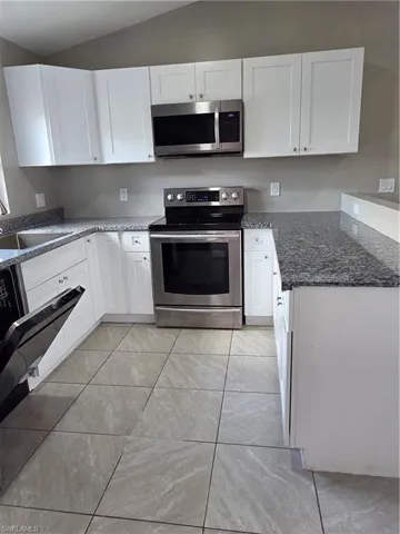 Kitchen featuring stainless steel electric stove, white cabinets, vaulted ceiling, and dark stone counters