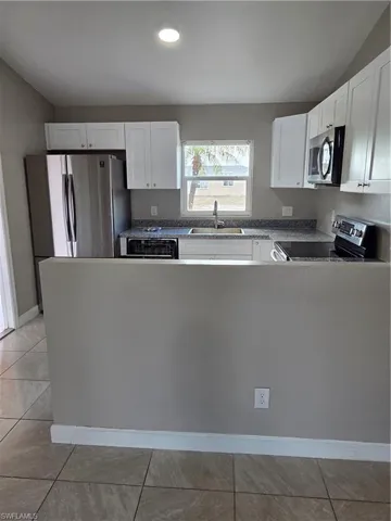 Kitchen with range, white cabinets, a peninsula, stainless steel dishwasher, and vaulted ceiling