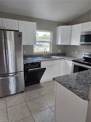 Kitchen featuring refrigerator, range, white cabinets, dishwashing machine, and vaulted ceiling