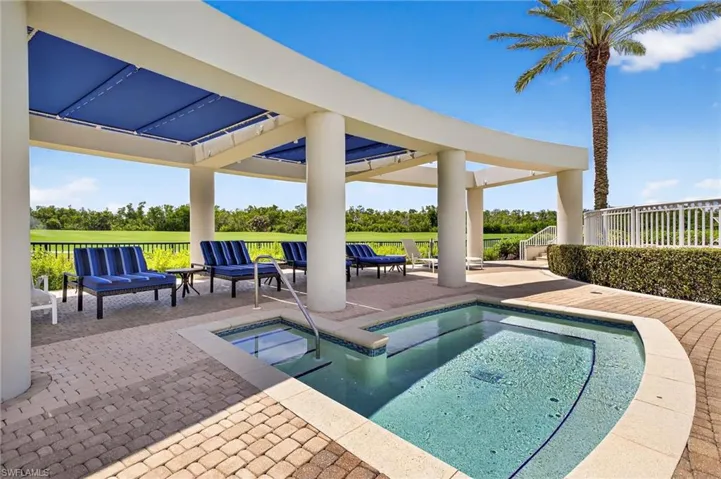 Outdoor pool featuring an in-ground hot tub, a patio, and view of scattered trees