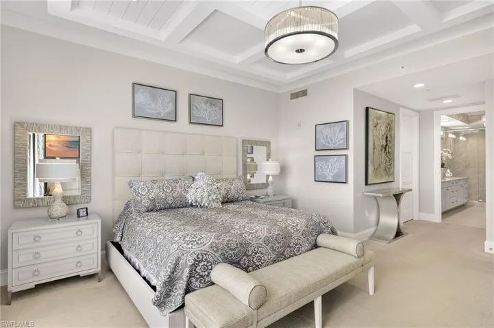 Bedroom featuring light colored carpet, beamed ceiling, coffered ceiling, and ensuite bathroom