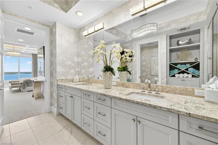 Ensuite bathroom with double vanity, a stall shower, light marble finish floors, a water view, and recessed lighting