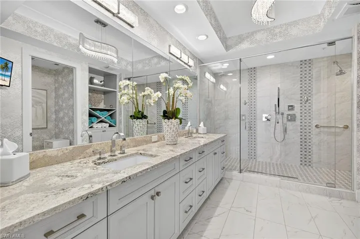Full bath with double vanity, a stall shower, light marble finish flooring, a raised ceiling, and recessed lighting