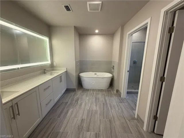 Bathroom featuring a dual vanity with light-colored countertops, an illuminated mirror, a freestanding soaking tub, and a separate shower with a glass enclosure