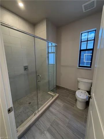 Bathroom featuring a glass-enclosed shower with tiled walls and floor, a toilet, and light-colored tiled flooring