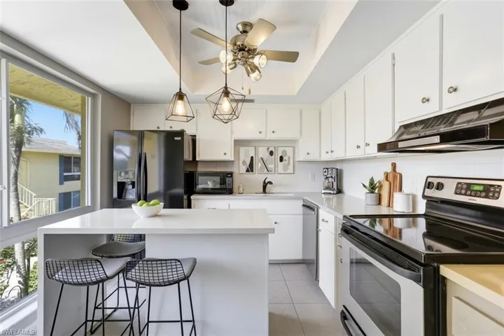 355-Palm-Dr-732-Naples-FL-Kitchen-virtual staged- featuring black appliances, light countertops, white cabinetry, a kitchen island, and hanging light fixtures