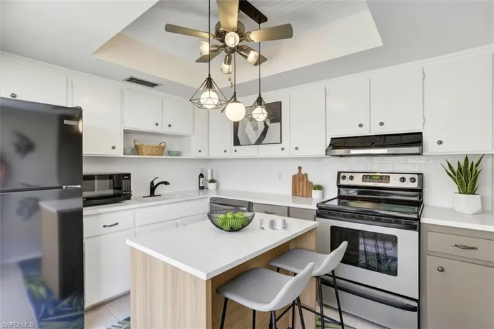 355-Palm-Dr-732-Naples-FL-virtual staged kitchen featuring black appliances, backsplash, open shelves, dual tone cabinets, and a breakfast bar
