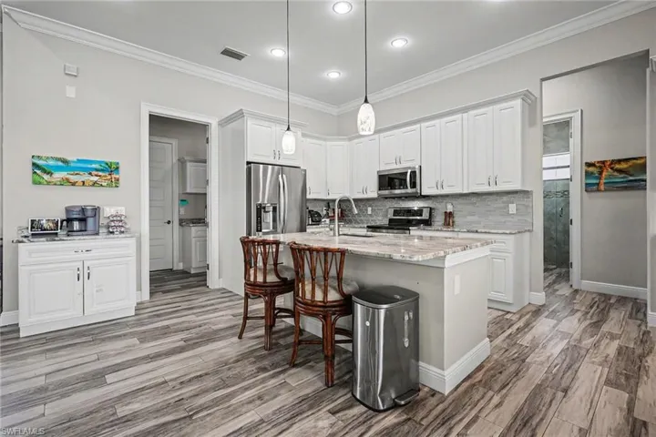 Kitchen with white cabinets, stainless steel appliances, crown molding, light stone counters, and decorative light fixtures