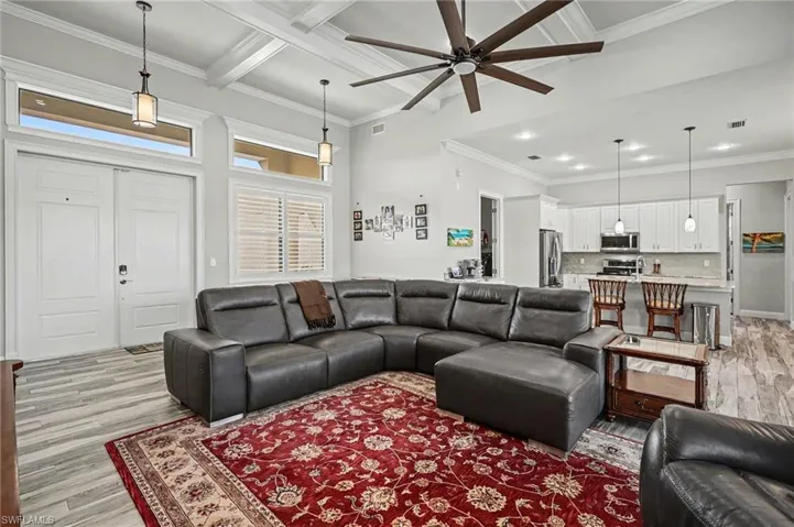 Living room with light wood finished floors, ornamental molding, ceiling fan, and coffered ceiling
