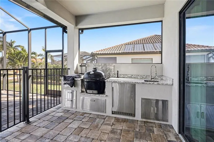 View of patio featuring exterior kitchen, a sunroom, and glass enclosure