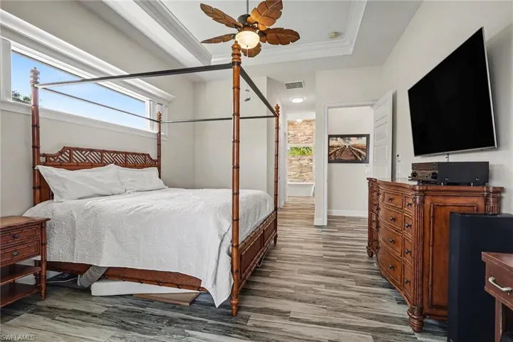 Bedroom featuring ceiling fan, wood finished floors, crown molding, and a raised ceiling