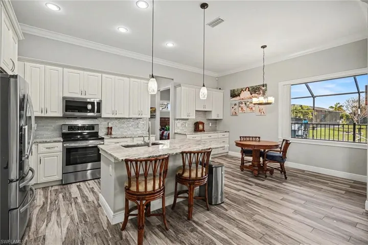 Kitchen with stainless steel appliances, pendant lighting, crown molding, light stone counters, and white cabinets