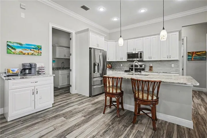 Kitchen with light stone countertops, stainless steel appliances, pendant lighting, ornamental molding, and white cabinets