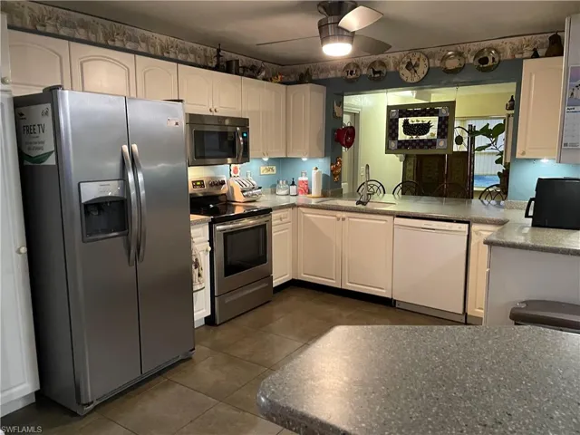 Kitchen with white cabinets, a ceiling fan, dark tile patterned flooring, and appliances with stainless steel finishes