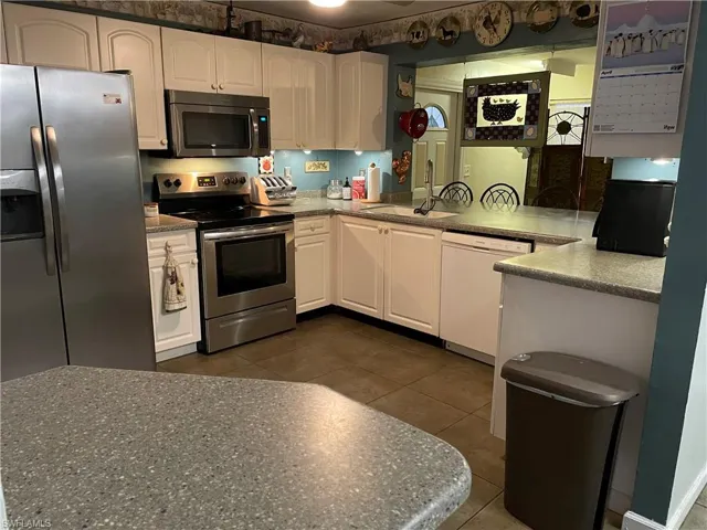 Kitchen featuring appliances with stainless steel finishes, white cabinetry, dark tile patterned flooring, and a sink