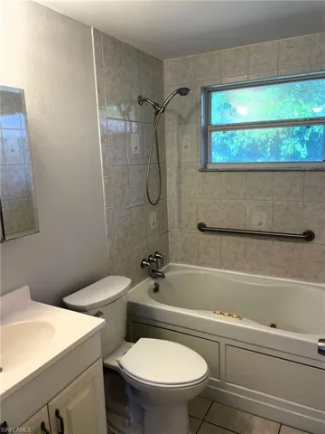 Bathroom featuring vanity, a combined bath / shower with jetted tub, a textured wall, and light tile patterned floors