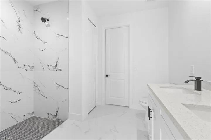 Bathroom featuring a tile shower, vanity, and toilet