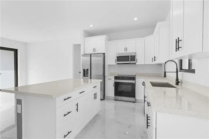 Kitchen with sink, light stone counters, a center island, appliances with stainless steel finishes, and white cabinets