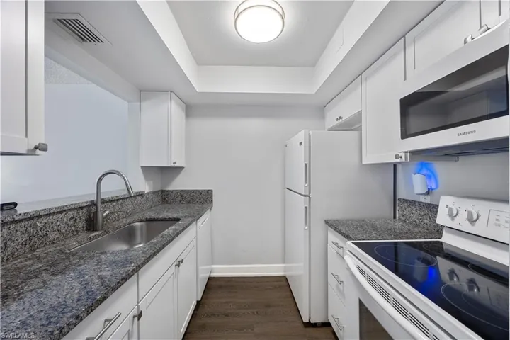 Kitchen with granite countertops, white cabinets and appliances with vinyl flooring.