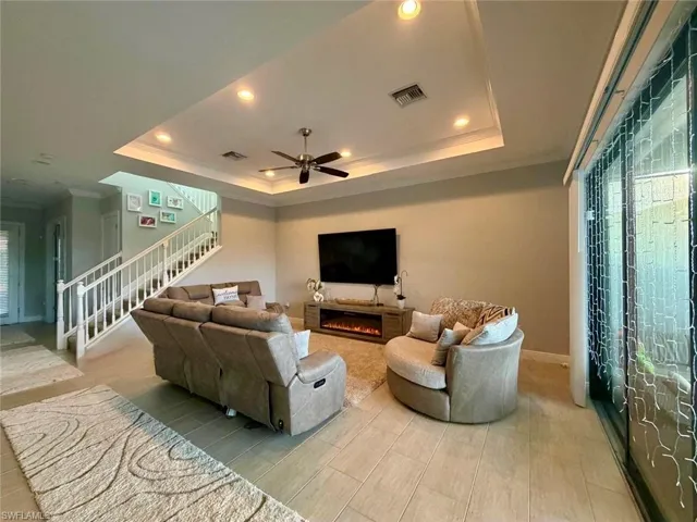 Living room with crown molding, recessed lighting, ceiling fan, stairs, and a warm lit fireplace