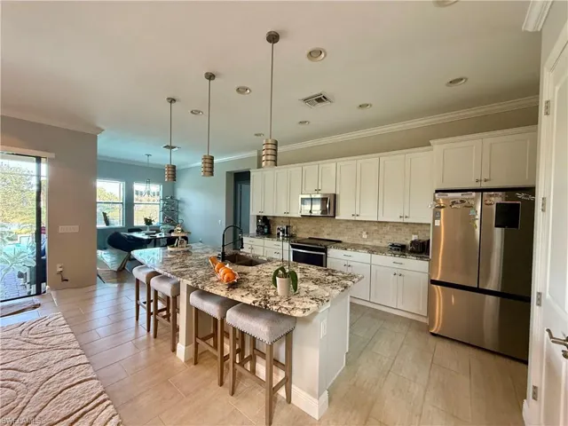 Kitchen with a breakfast bar area, appliances with stainless steel finishes, crown molding, white cabinetry, and a kitchen island with sink