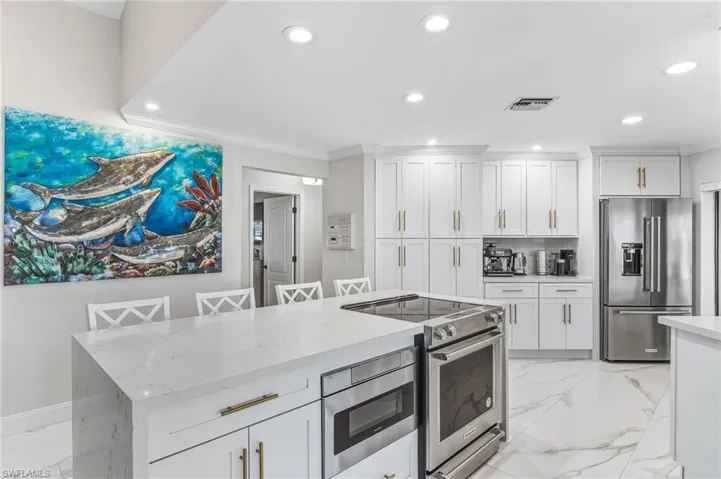 Kitchen with light marble finish floors, stainless steel appliances, a breakfast bar area, white cabinets, and ornamental molding