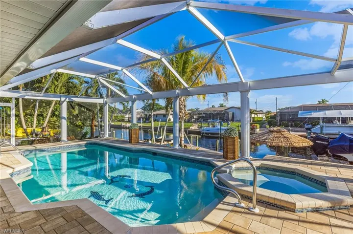 Swimming pool with boat lift, a water view, a lanai, and an in-ground hot tub