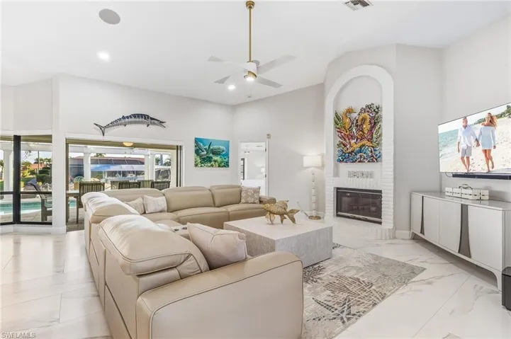 Living area featuring ceiling fan, a fireplace, light marble finish flooring, high vaulted ceiling, and recessed lighting