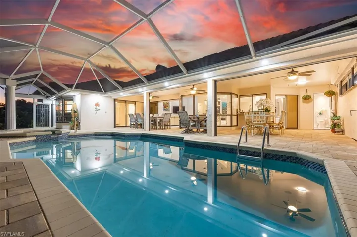 Pool at dusk with a pool with connected hot tub and a sunroom