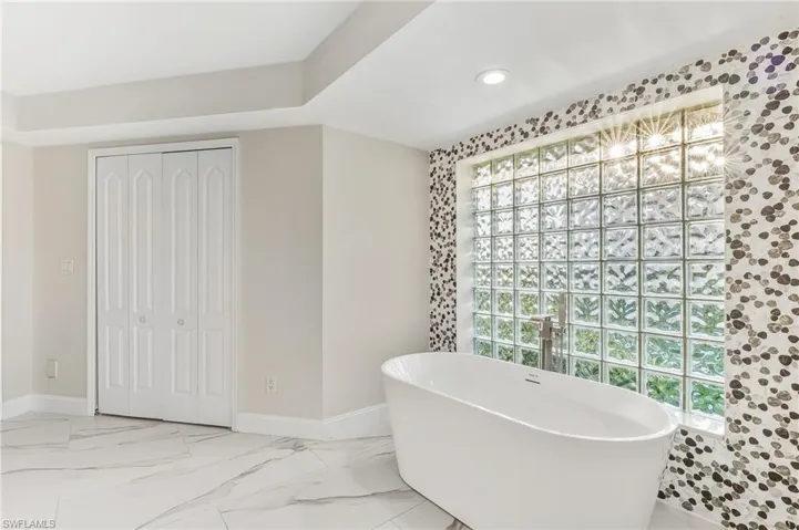 Full bathroom featuring a freestanding bath, a closet, light marble finish flooring, plenty of natural light, and recessed lighting