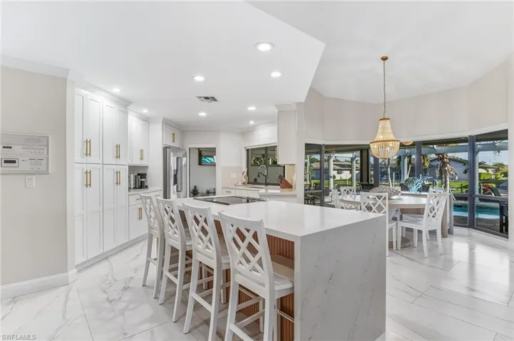 Kitchen featuring a breakfast bar area, healthy amount of natural light, white cabinets, light marble finish floors, and ornamental molding