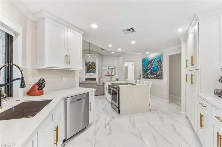 Kitchen with light stone counters, appliances with stainless steel finishes, white cabinets, crown molding, and a kitchen island