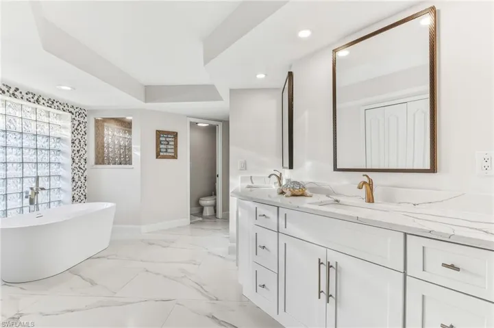 Bathroom featuring double vanity, a soaking tub, recessed lighting, and light marble finish flooring