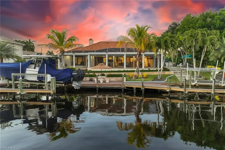Back of house at dusk with boat lift, a water view, a lanai, and a patio area