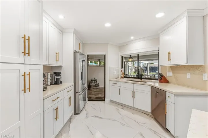 Kitchen with crown molding, appliances with stainless steel finishes, white cabinetry, light marble finish floors, and recessed lighting