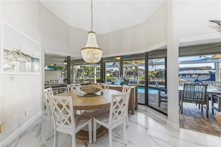 Dining space with a sunroom, a water view, a ceiling fan, and light marble finish floors