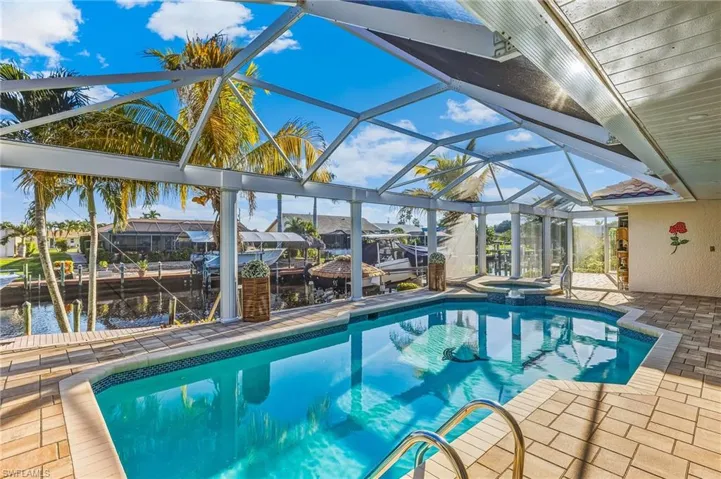 View of swimming pool with a sunroom, a patio, glass enclosure, boat lift, and a pool with connected hot tub