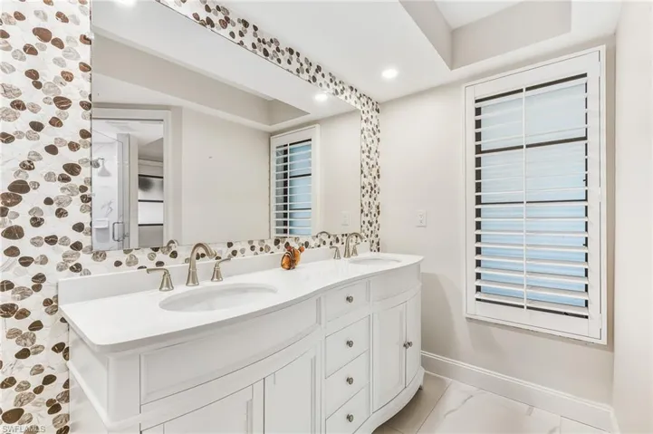 Bathroom with double vanity, recessed lighting, and light marble finish flooring