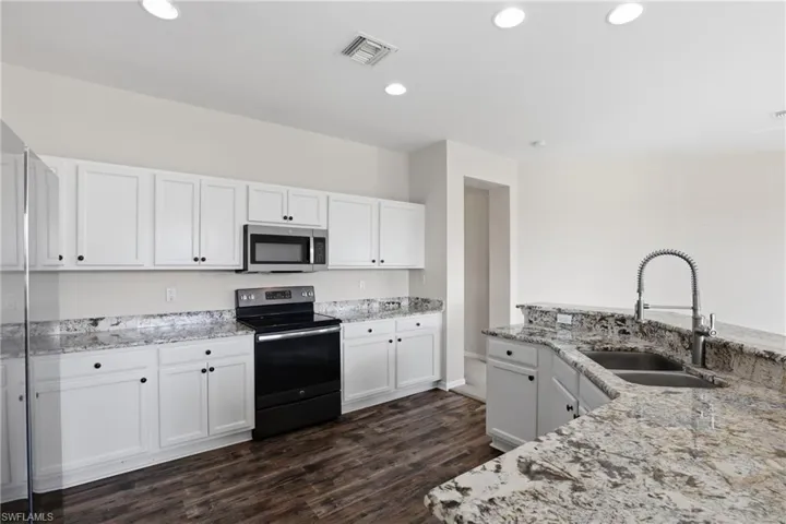 Kitchen with stainless steel appliances, white cabinets, dark wood finished floors, light stone countertops, and recessed lighting