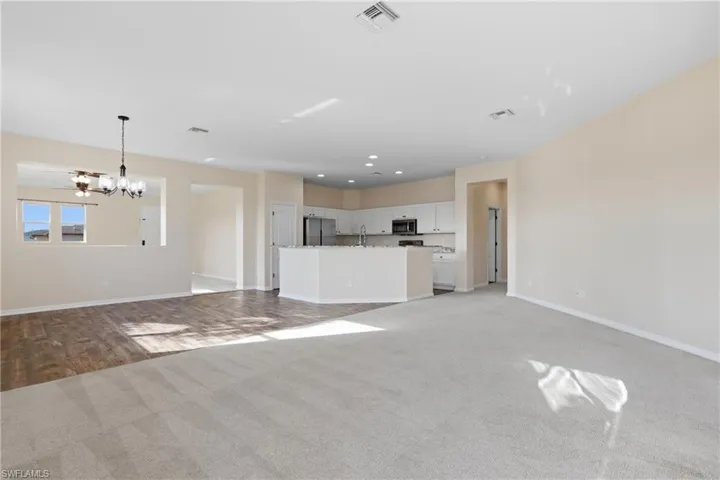 Unfurnished living room with light colored carpet and a chandelier
