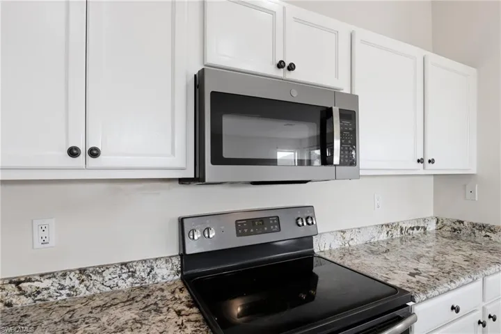Kitchen with stainless steel appliances, white cabinets, and light stone countertops