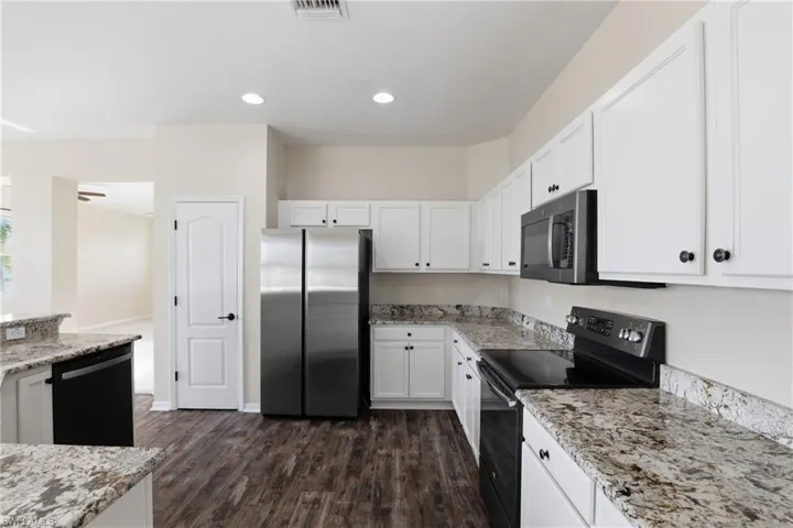 Kitchen featuring black appliances, light stone countertops, white cabinetry, dark wood-style floors, and recessed lighting
