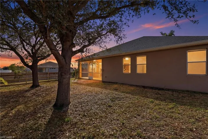 Back of house at dusk featuring a sunroom, roof with shingles, and stucco siding
