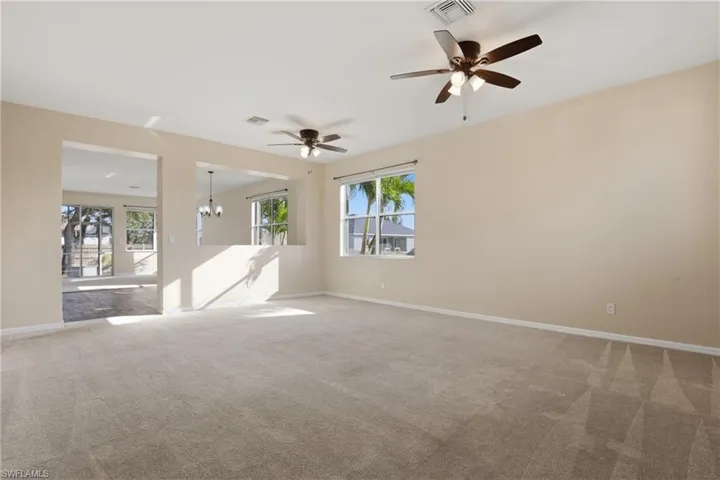 Carpeted spare room featuring healthy amount of natural light, a ceiling fan, and hanging lights