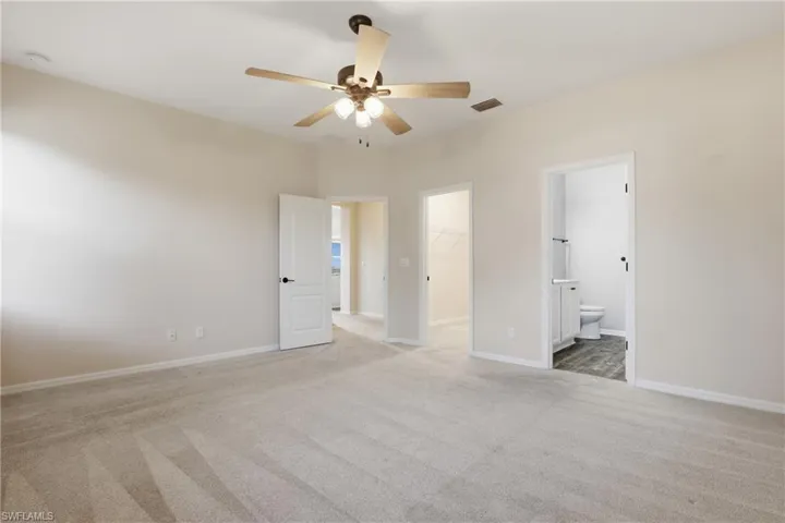 Unfurnished bedroom with light carpet, a walk in closet, a ceiling fan, and ensuite bath