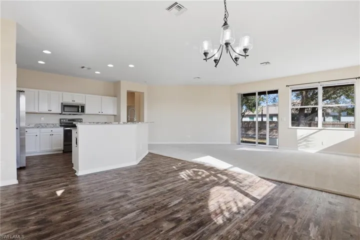 Unfurnished living room with dark wood-type flooring and hanging lights